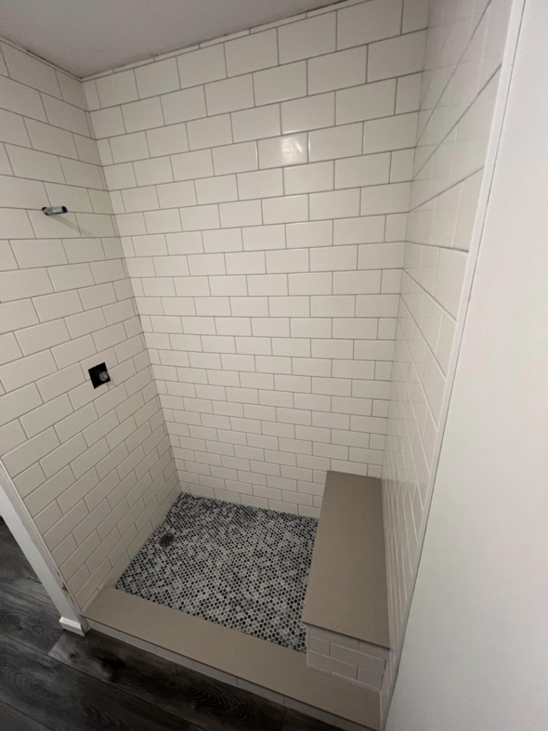 Detailed view of walk-in shower tiling with white subway tiles and a built-in bench by Roempagel Renovations LLC in South Bend, IN.