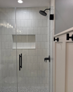 A modern walk-in tiled shower with a clear glass door, black fixtures, and a built-in niche by Valley Wide Design & Build in San Tan Valley, AZ.