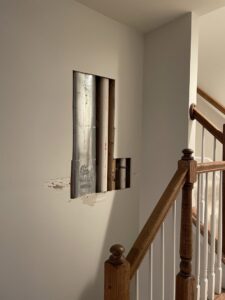 A wall with a cutout exposing pipes and ducts, indicating a repair or access project by N. Bennecoff Drywall & Plaster in Lancaster, PA.