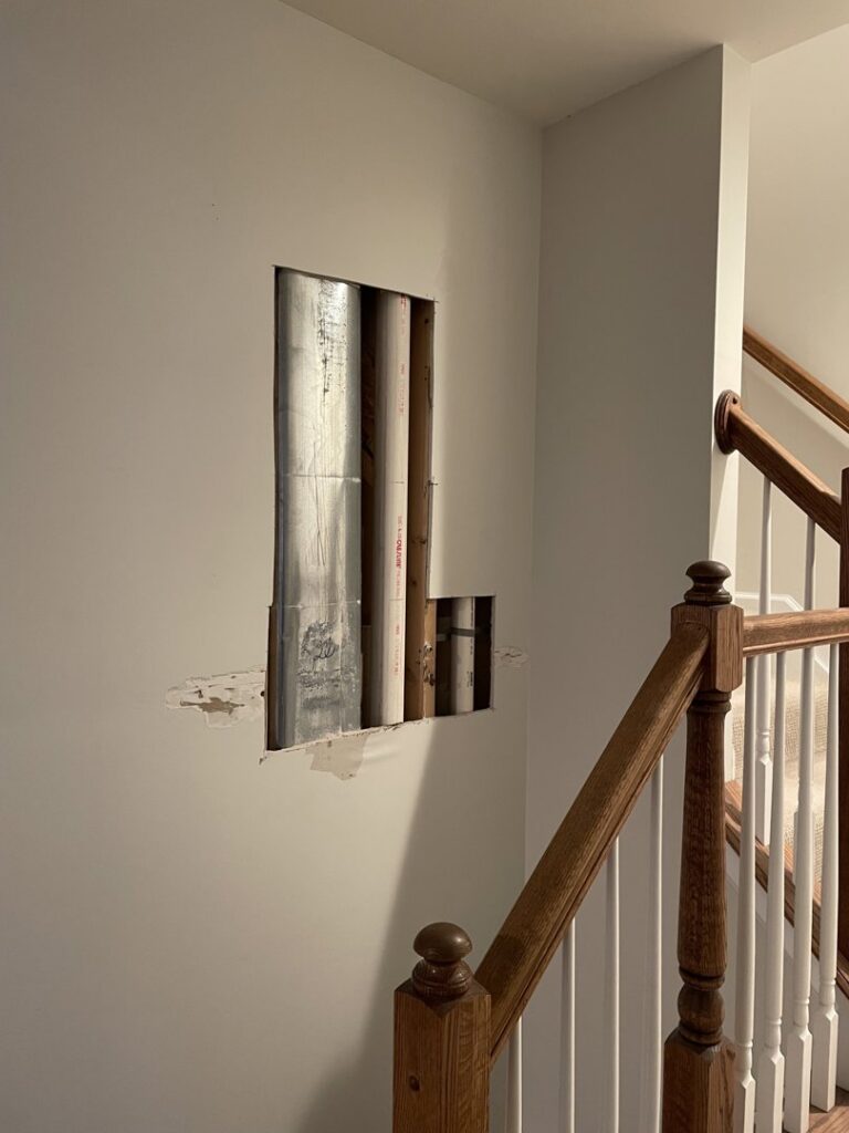A wall with a cutout exposing pipes and ducts, indicating a repair or access project by N. Bennecoff Drywall & Plaster in Lancaster, PA.