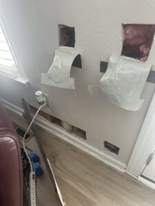 A wall with holes cut out for drywall repair, exposing insulation and wiring by Castle Drywall & Plaster in Chesapeake, VA.