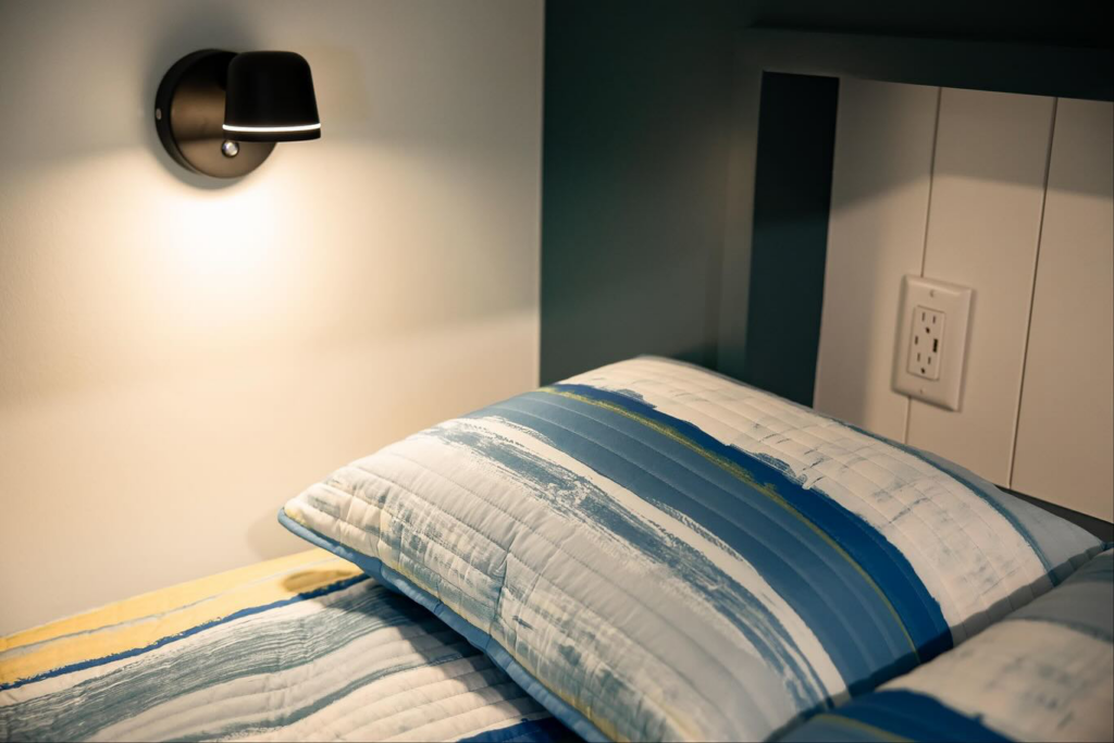 A newly installed wall-mounted light fixture and electrical outlet next to a bed by An Extra Hand in Indianapolis, IN.