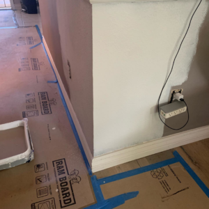 A close-up of a wall painting in progress with a paint tray and floor protection by Island Handyman in Honolulu, HI.