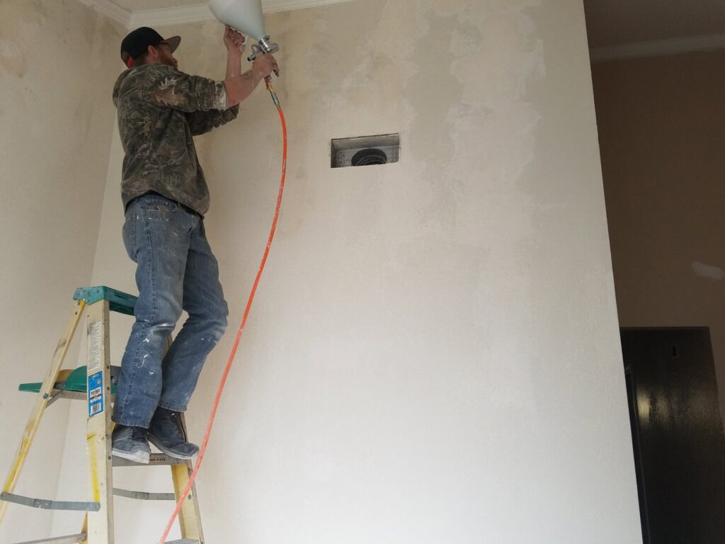 A contractor on a ladder spraying texture onto a wall for Red Gator Maintenance in Fresno, CA.
