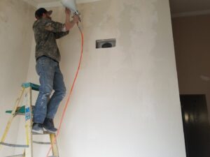 A contractor on a ladder spraying texture onto a wall for Red Gator Maintenance in Fresno, CA.