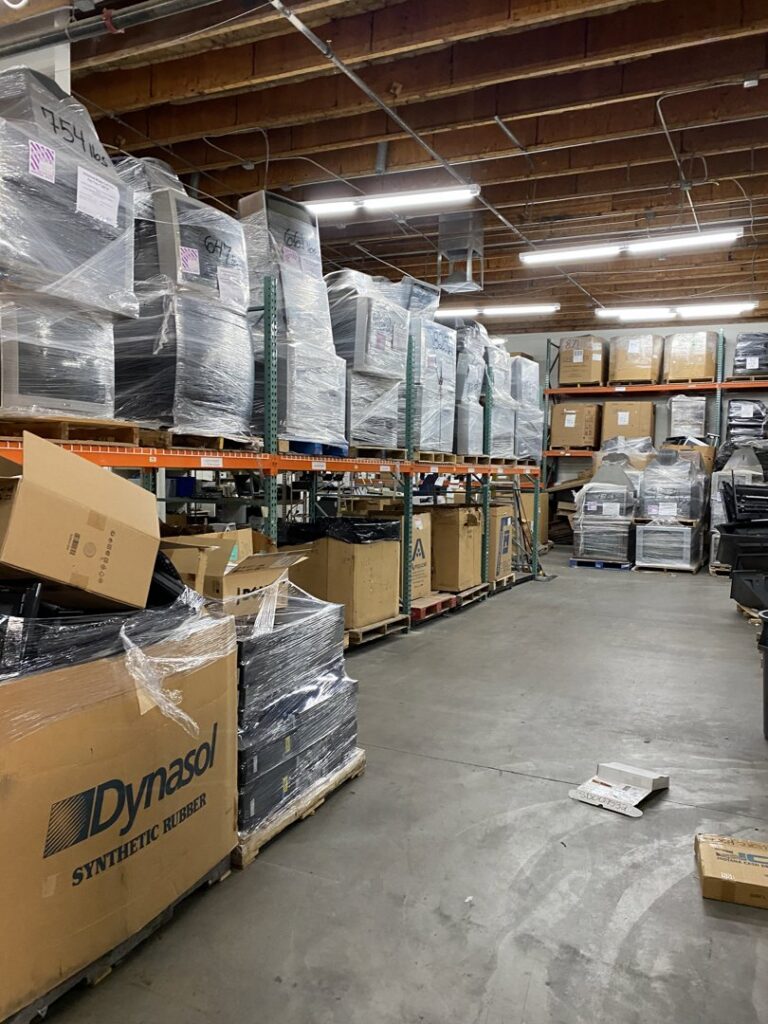 A warehouse aisle with pallets stacked high with shrink-wrapped e-waste at R3Ewaste in Phoenix, AZ