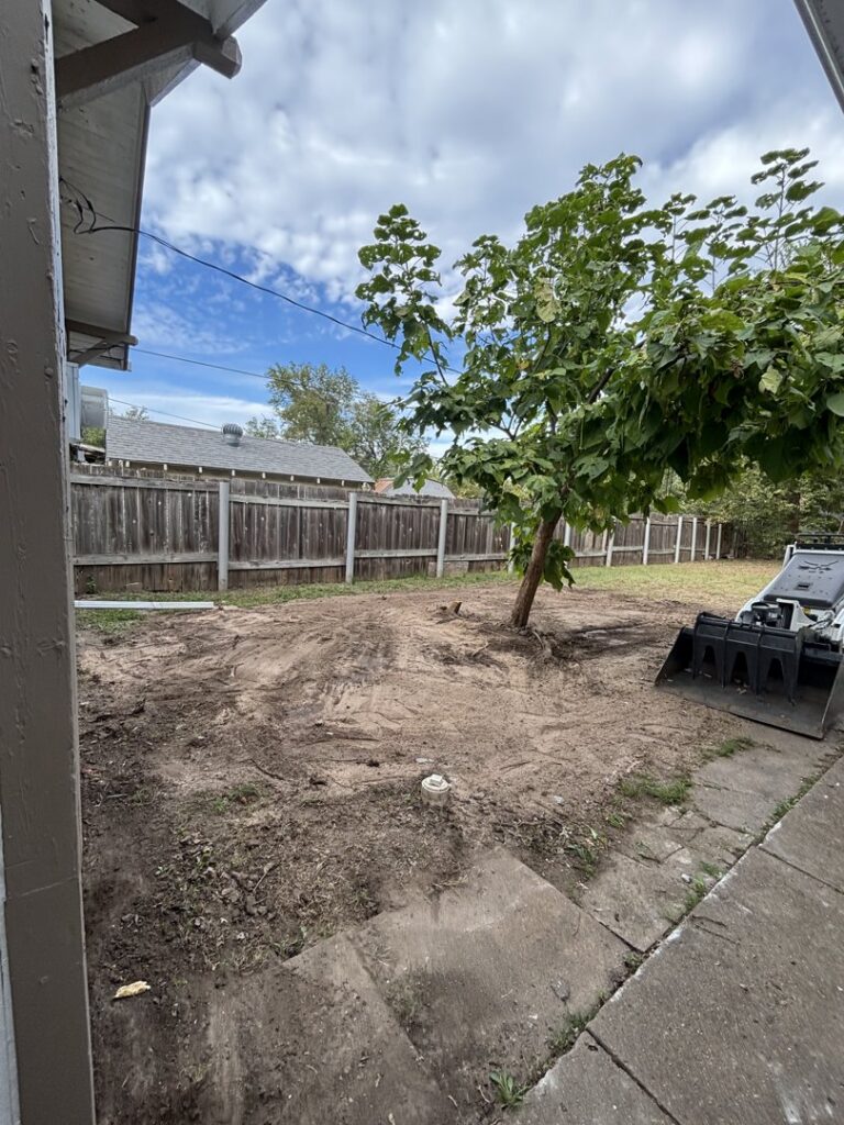 A backyard cleared of debris and overgrowth, with an excavator visible, by Waste Warrior in Wichita, KS.