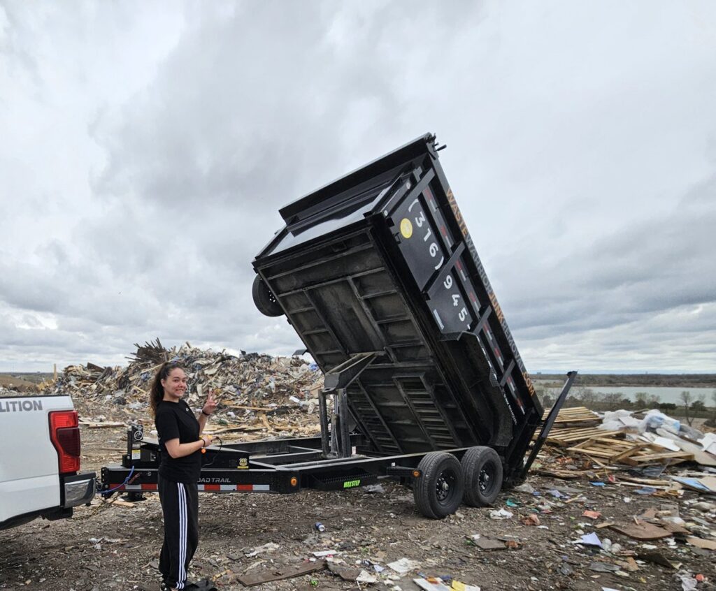 A Waste Warrior dump trailer unloading debris next to a large junk pile, with a team member, in Wichita, KS.