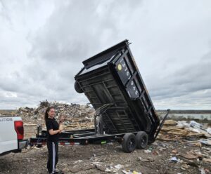 A Waste Warrior dump trailer unloading debris next to a large junk pile, with a team member, in Wichita, KS.