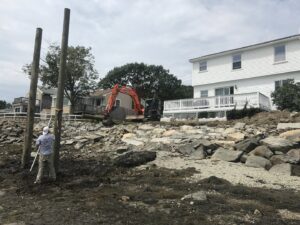 A worker installing wooden pilings for a waterfront structure with an excavator in the background by Solimini Excavation and Utility in Freetown, MA