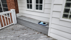 A weathered wooden deck with a clipboard and phone, suggesting an assessment for repair or maintenance by Sundecks, Inc. in Manassas, VA.