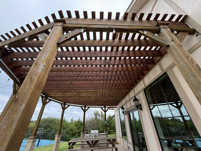 A weathered wooden pergola attached to a building, showing potential for maintenance by Oklahoma Painting & Construction in Oklahoma City, OK.