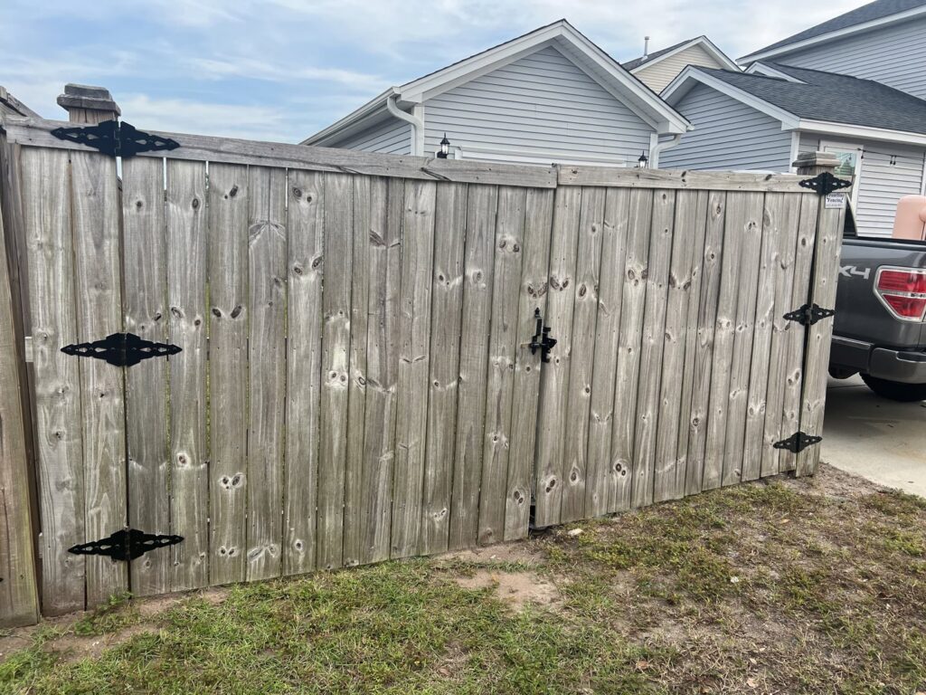A weathered wooden fence with a gate featuring decorative black hinges and latch, showing the quality of work by Frontline Fencing LLC in Summerville, SC.