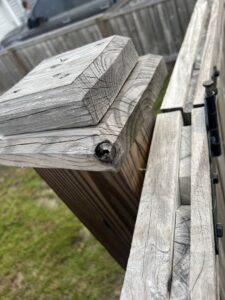 A close-up view of a weathered wooden fence post and gate hinge, showing potential repair or maintenance work by Frontline Fencing LLC in Summerville, SC.