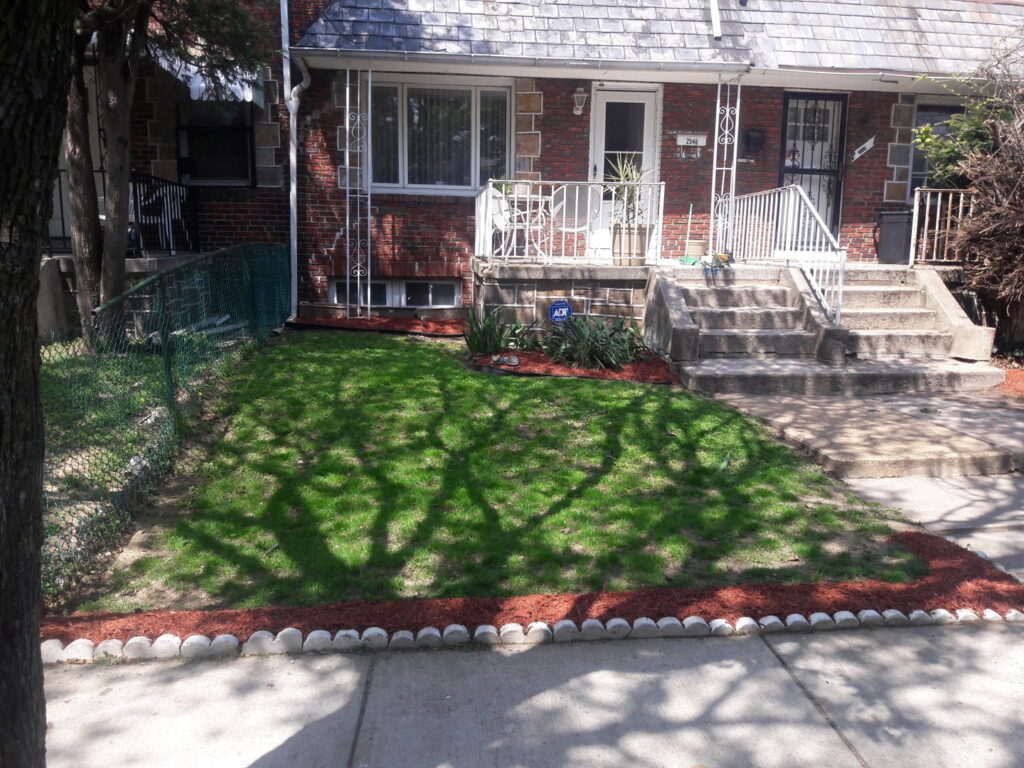 A well-maintained front yard with a green lawn and dark mulched garden beds, by C&C LAWN CARE,MOVING & TRASH REMOVAL in Baltimore, MD