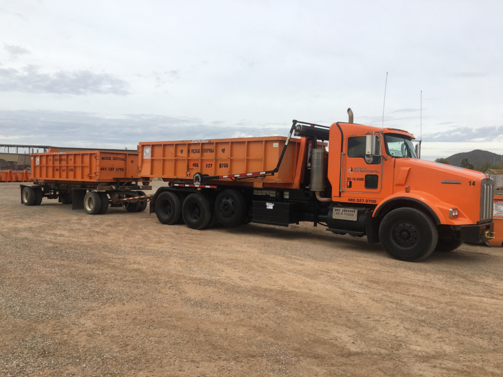 An orange Wesco Disposal truck with two large roll-off dumpsters ready for junk removal in Phoenix, AZ.