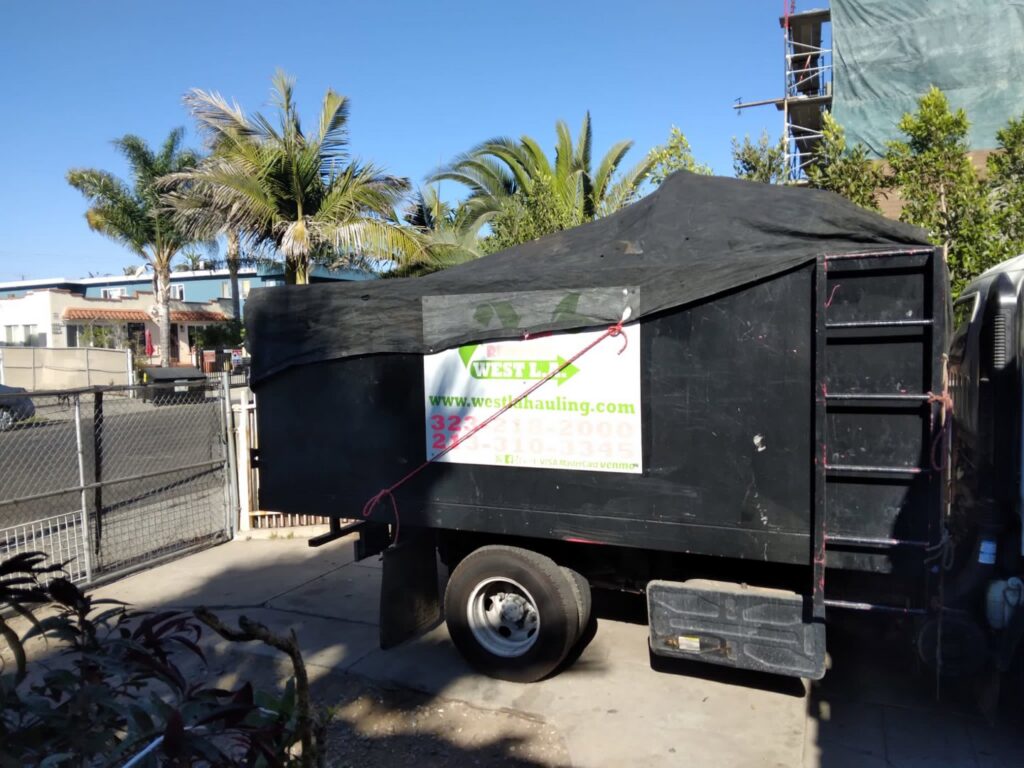 A black West LA Hauling junk removal truck with a tarp covering the load in Los Angeles, CA.
