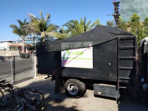 A black West LA Hauling junk removal truck with a tarp covering the load in Los Angeles, CA.