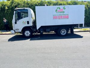 A white junk removal truck with West LA Hauling branding parked on a street in Los Angeles, CA.