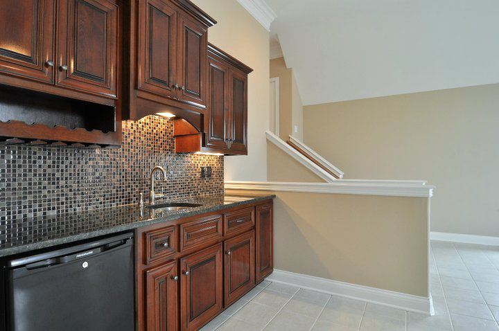 A newly installed wet bar with dark wood cabinets, mosaic tile backsplash, and a sink by Nixon Construction in Nashville, TN.