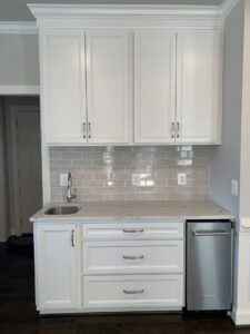 Newly installed wet bar with white cabinets and a stainless steel dishwasher by Quaker Custom Homes, LLC in Woodbridge, VA
