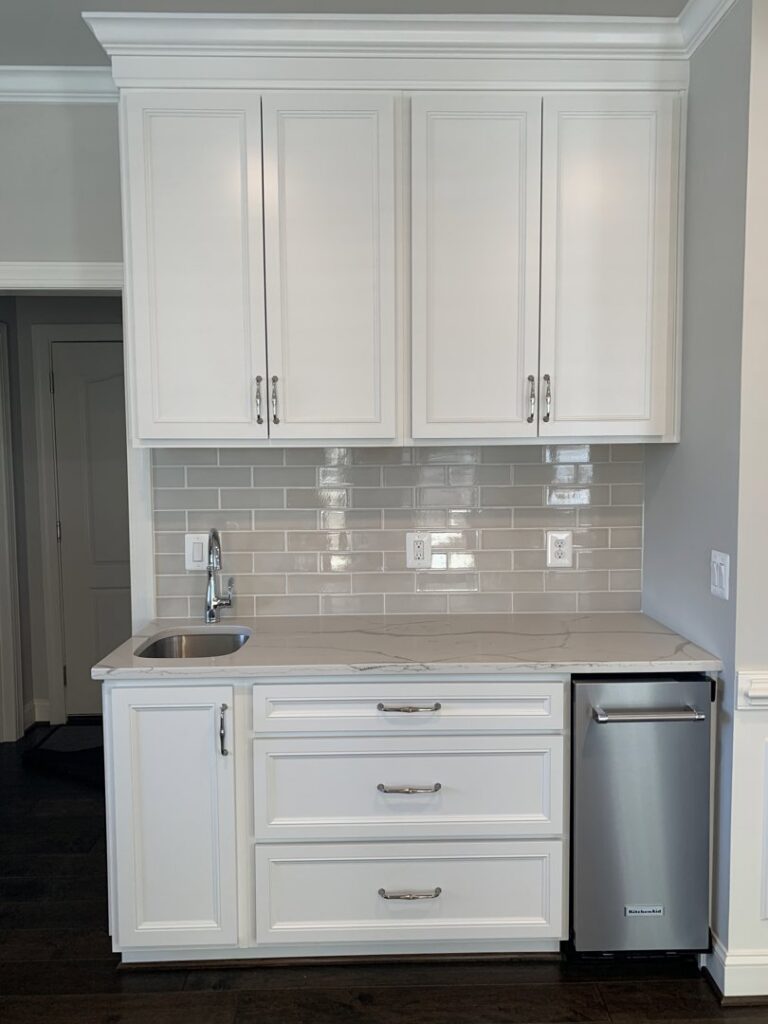 Newly installed wet bar with white cabinets and a stainless steel dishwasher by Quaker Custom Homes, LLC in Woodbridge, VA