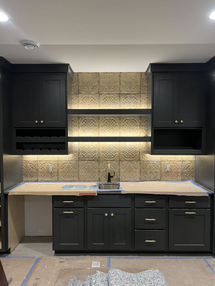 A newly installed wet bar with dark cabinets, a sink, and a decorative backsplash by Tri Lake Construction in Madison, WI