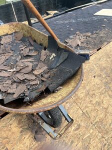 A wheelbarrow filled with roofing debris next to a dump trailer for Silverback Dumpster Rentals in LaBelle, FL.