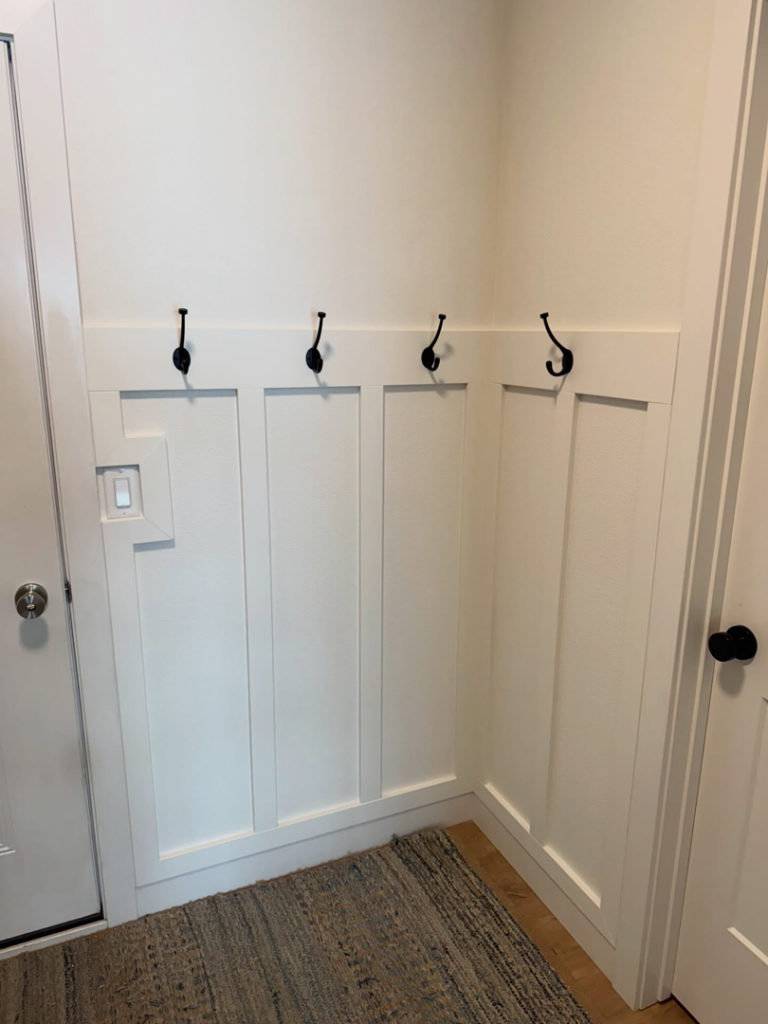 White board and batten wainscoting with black coat hooks installed in an entryway by LIV Custom Accents in West Fargo, ND