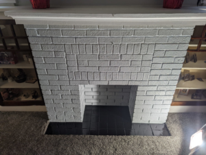 A beautifully painted white brick fireplace with a black tiled hearth by Imagine Painting and Restoration Services in Fort Collins, CO.