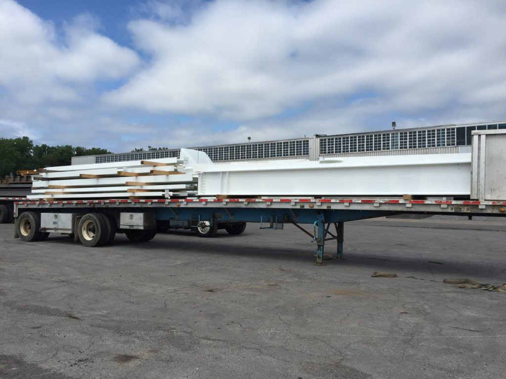 White coated structural steel beams loaded on a flatbed trailer for transport by Carpenter Industries Inc. in Syracuse, NY.