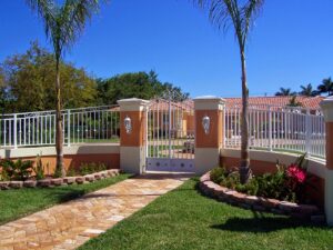 White decorative fence and gate with stucco pillars installed by Xclusive Fence And Rails Inc. in Miami, FL.
