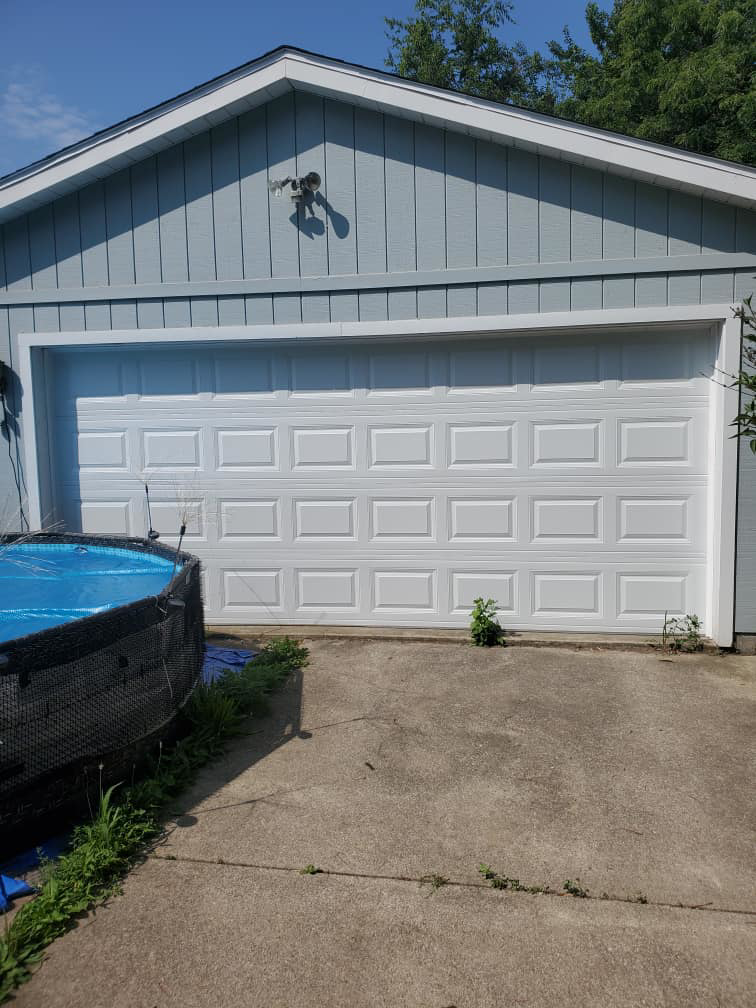 A newly installed white garage door on a home with light blue siding by Lucas Overhead Doors, a general contractor in Erie, PA