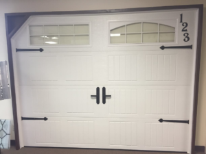 A white garage door with arched windows and black decorative hardware, a product of Harold Carpenter Overhead Door inc in Oshkosh, WI.