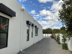 A white house featuring black window awnings for sun protection and a white rain gutter downspout, installed by Phoenix Rain Gutters and Sun Protection in Glendale, AZ.