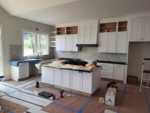 White kitchen cabinet and island installation in progress with tools and materials by Woods Builders in Grand Rapids, MI.