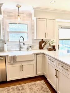 A kitchen with white refaced cabinets, dark countertops, and a farmhouse sink by Cincinnati Cabinet Refacing in Cincinnati, OH.
