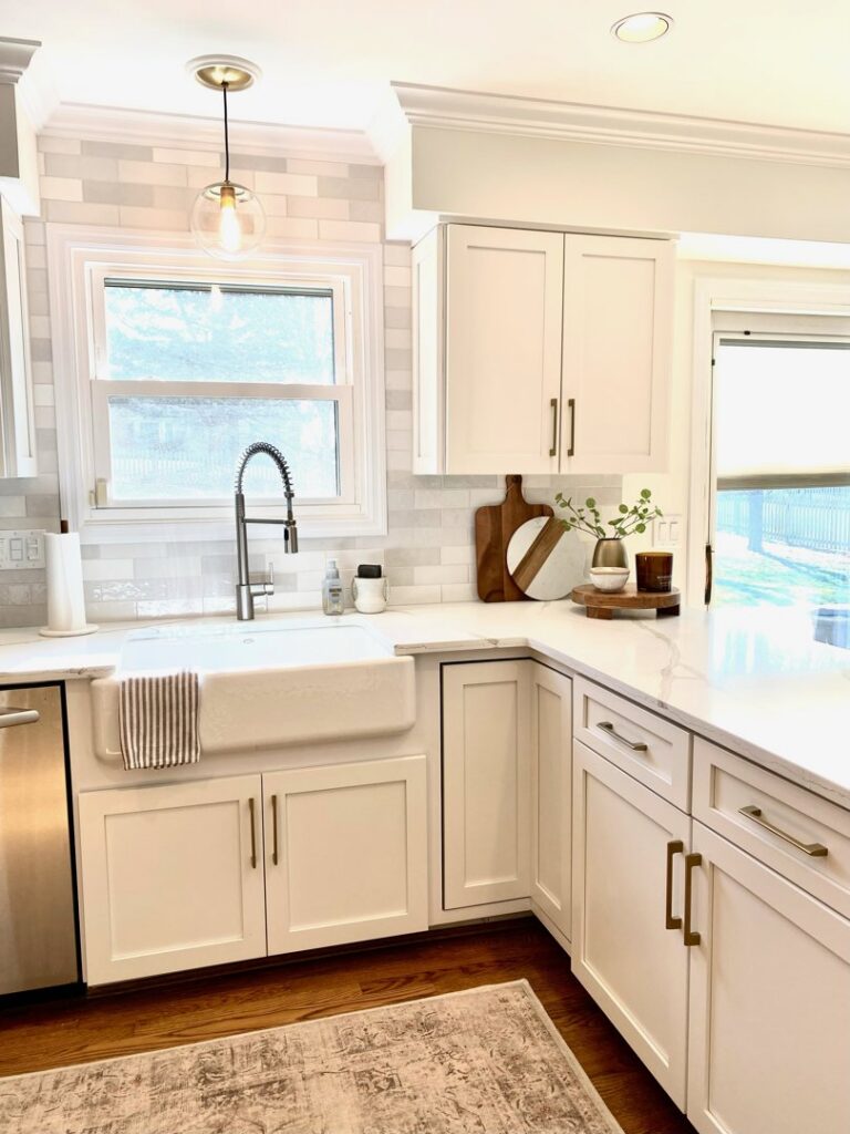 A kitchen with white refaced cabinets, dark countertops, and a farmhouse sink by Cincinnati Cabinet Refacing in Cincinnati, OH.