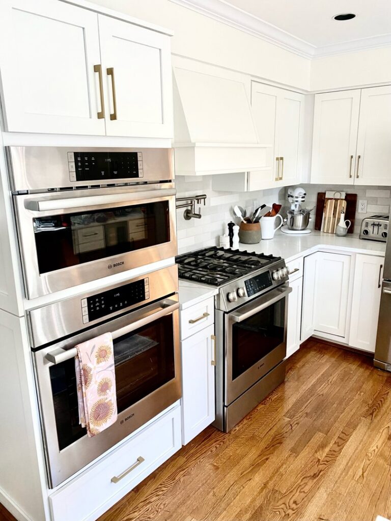 A kitchen featuring elegant white cabinets with gold hardware and built-in ovens, completed by Cincinnati Cabinet Refacing in Cincinnati, OH.