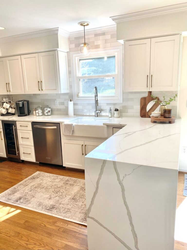 A bright kitchen featuring white cabinets, a farmhouse sink, and a light subway tile backsplash by Cincinnati Cabinet Refacing in Cincinnati, OH.