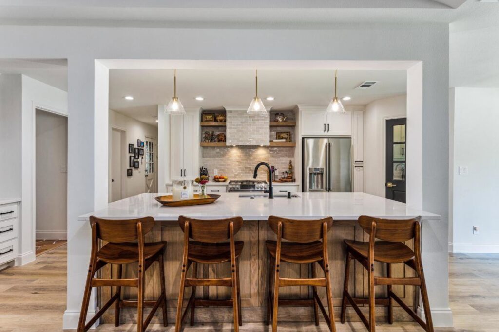 A renovated kitchen featuring white cabinets, a large range hood, and stainless steel appliances by DFW Improved in Plano, TX.