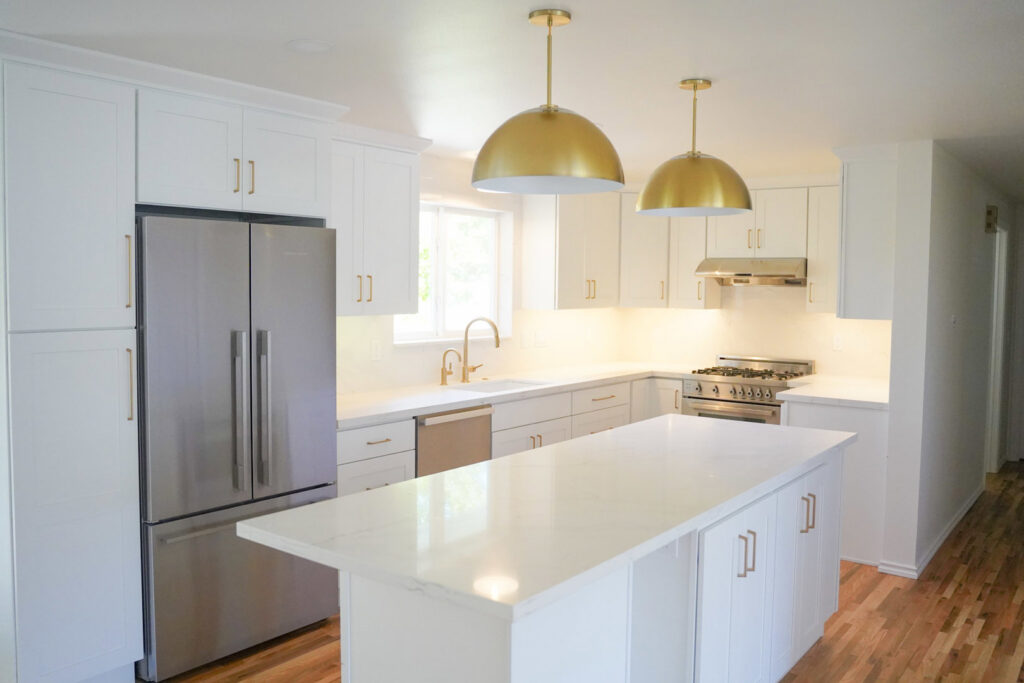 A stunning white kitchen remodel with gold pendant lights and stainless steel appliances by Gordon T. Jacob in Tacoma, WA