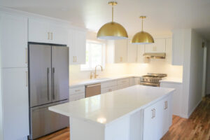 A stunning white kitchen remodel with gold pendant lights and stainless steel appliances by Gordon T. Jacob in Tacoma, WA