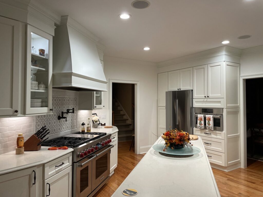 A beautifully remodeled white kitchen featuring a large island with a light countertop and stainless steel appliances by Pro Finishes NC, LLC in Raleigh, NC.