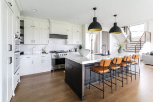A bright white kitchen with a dark island, subway tile backsplash, and modern pendant lights by DJK Custom Homes in Naperville, IL