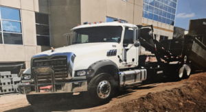 A white Mack roll-off truck with a large dumpster, ready for junk removal services by Stryker Environmental Inc in Bethel Dr., GA.