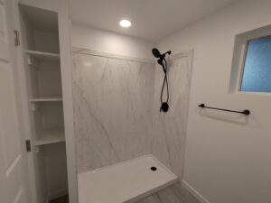 A newly installed shower with white marble-look wall panels and modern black fixtures, completed by Devco Construction LLC in West Valley City, UT.