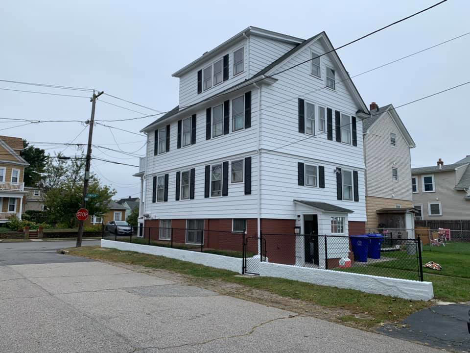 A white multi-story house exterior with a newly installed or painted fence by D'Costa Finish Painting in Fall River, MA.