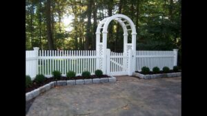 A charming white picket fence with an elegant arbor gate, installed by Fence Factory Inc in Stamford, CT