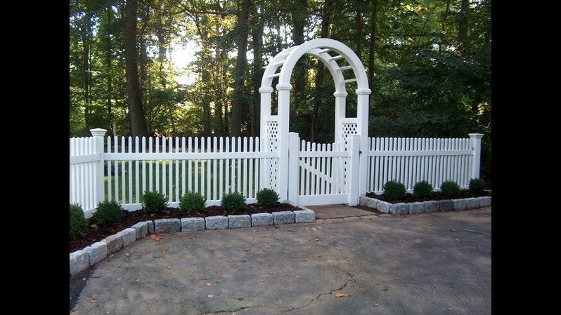 A charming white picket fence with an elegant arbor gate, installed by Fence Factory Inc in Stamford, CT